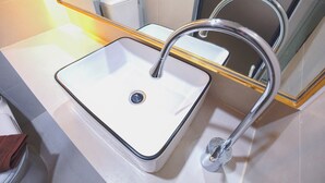 A bathroom with a white sink, chrome faucet, and a mirror with a gold frame. - RESET at DMK (Bangkok)