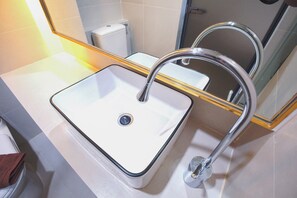Un baño con lavamanos blanco, grifo cromado y espejo con marco dorado.