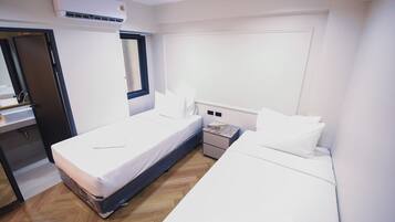Habitación de hotel con dos camas, una ventana, una mesita de noche, un equipo de aire acondicionado y piso de madera.