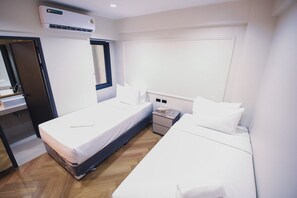 A hotel room with two beds, a window, a bedside table, an air conditioning unit, and a wooden floor. - RESET at DMK (Bangkok)