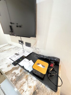 A flat-screen TV mounted on a wall, a remote control, a tissue box, and a pair of glasses on a marble countertop.