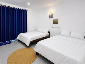 A hotel room with two single beds, a blue curtain, a welcome mat, and wall-mounted pictures.