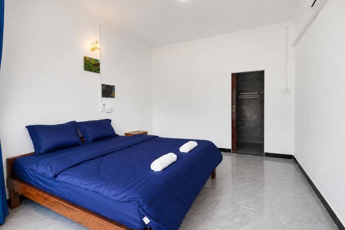 A bedroom with a wooden bed, white walls, a door, and a small nightstand.