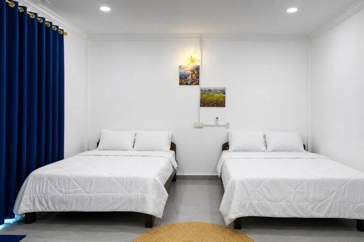 A room with two beds, a blue curtain, a wall-mounted light, and a small picture.