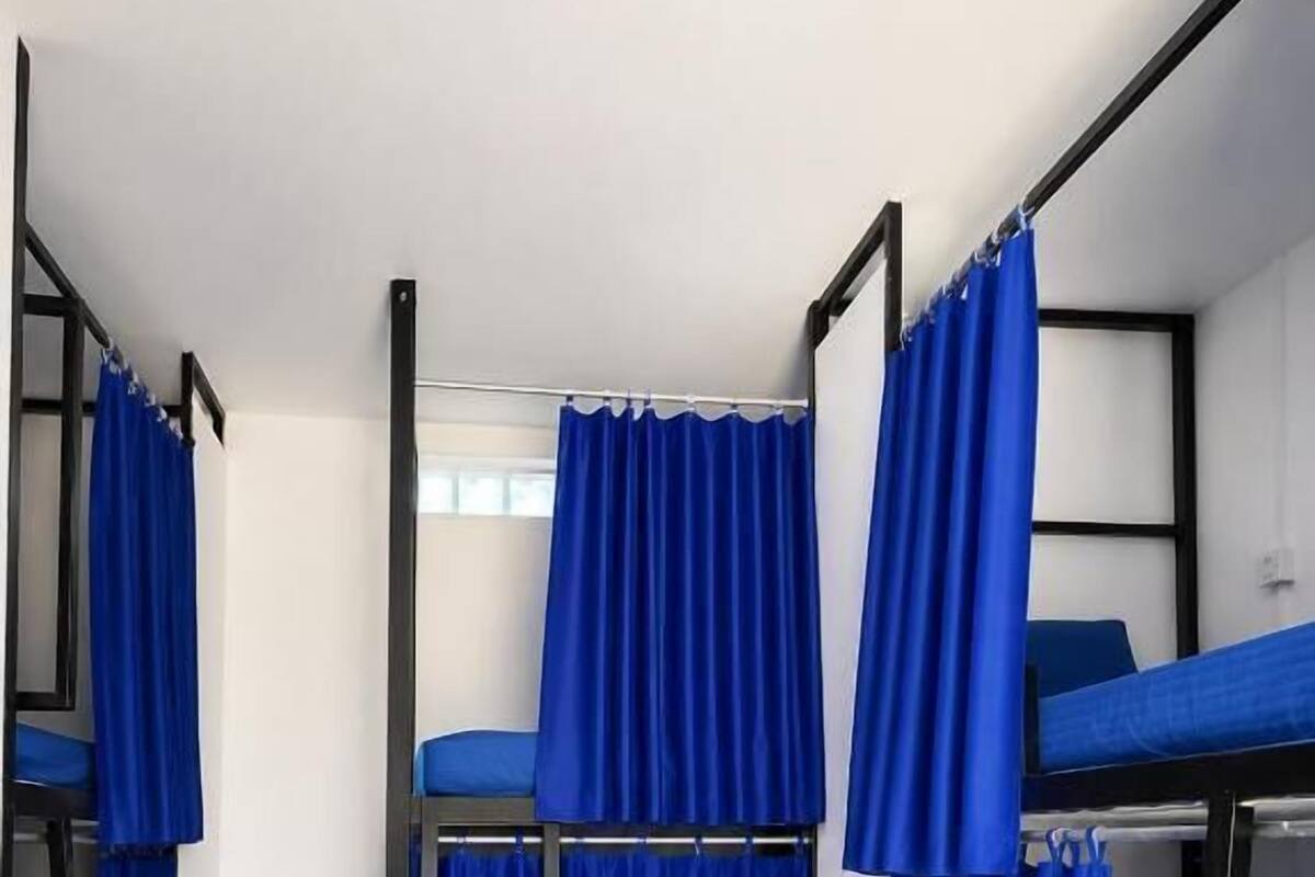 A dormitory room with bunk beds, a ladder, and blue curtains.