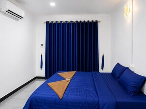A hotel room with a bed, a blue curtain, an air conditioning unit, and a wall-mounted light fixture. - David's Hostel & Restaurant (Koh Rong)