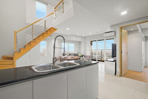 A modern kitchen with a wooden staircase, a dining area with a view, and a large window. - Magnolia by Kozystay - Kebon Jeruk (Jakarta Selatan)
