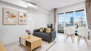 A modern living room with a grey sofa, a wooden coffee table, and a dining area with white chairs. - Magnolia by Kozystay - Kebon Jeruk (Jakarta Selatan)