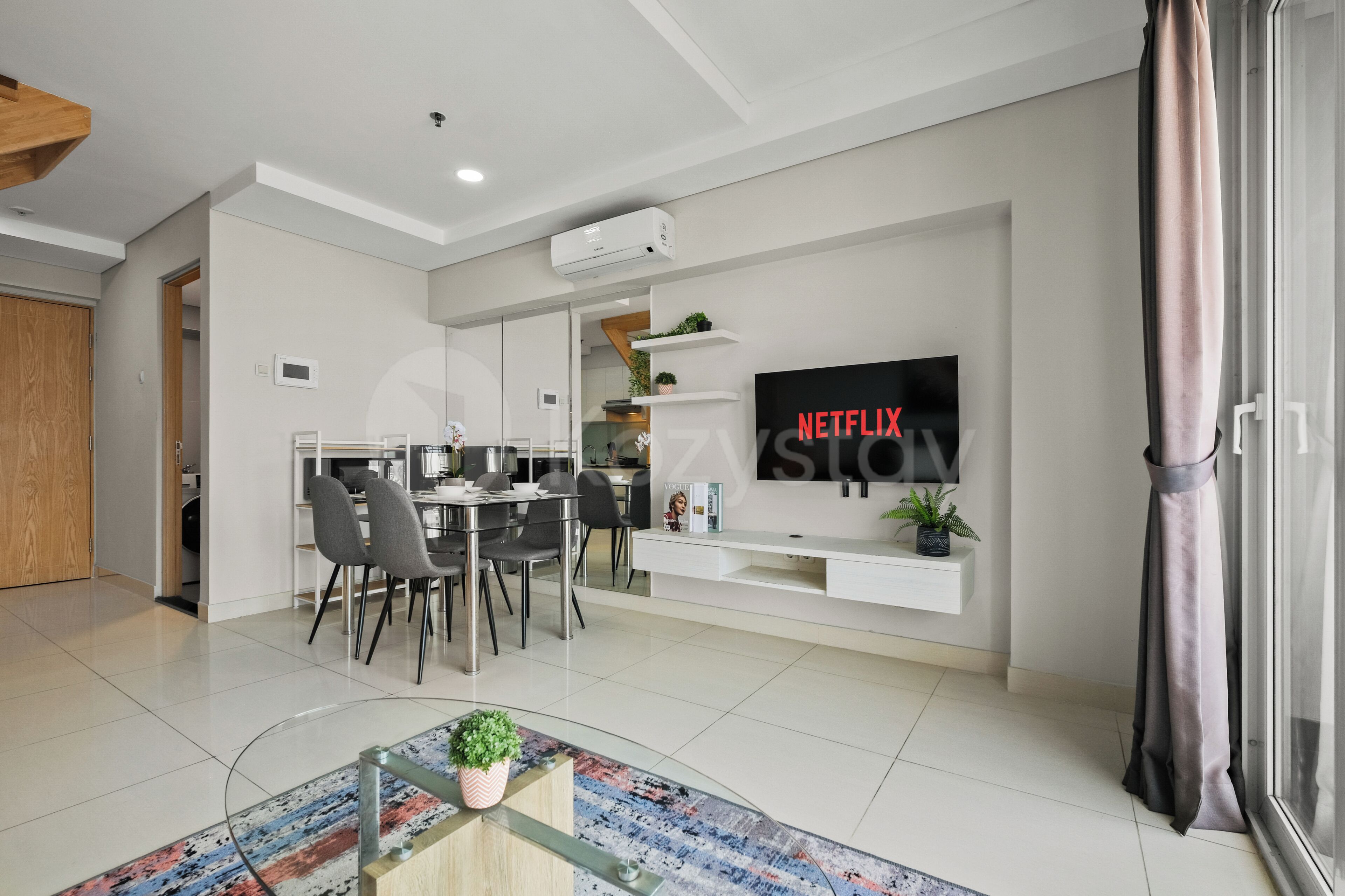 Un salon moderne comprenant un coin repas, un téléviseur fixé au mur et une table basse en verre.
