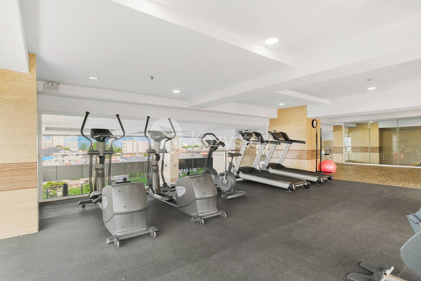 A gym with treadmills, elliptical machines, and a red exercise ball.