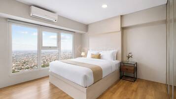 A modern bedroom with a large bed, a nightstand, a window with a city view, and an air conditioning unit.