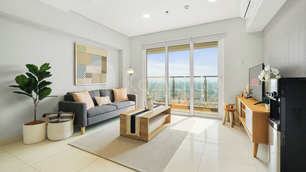 A modern living room with a sofa, coffee table, and a balcony with a city view. - Magnolia by Kozystay - Kebon Jeruk (Jakarta Selatan)