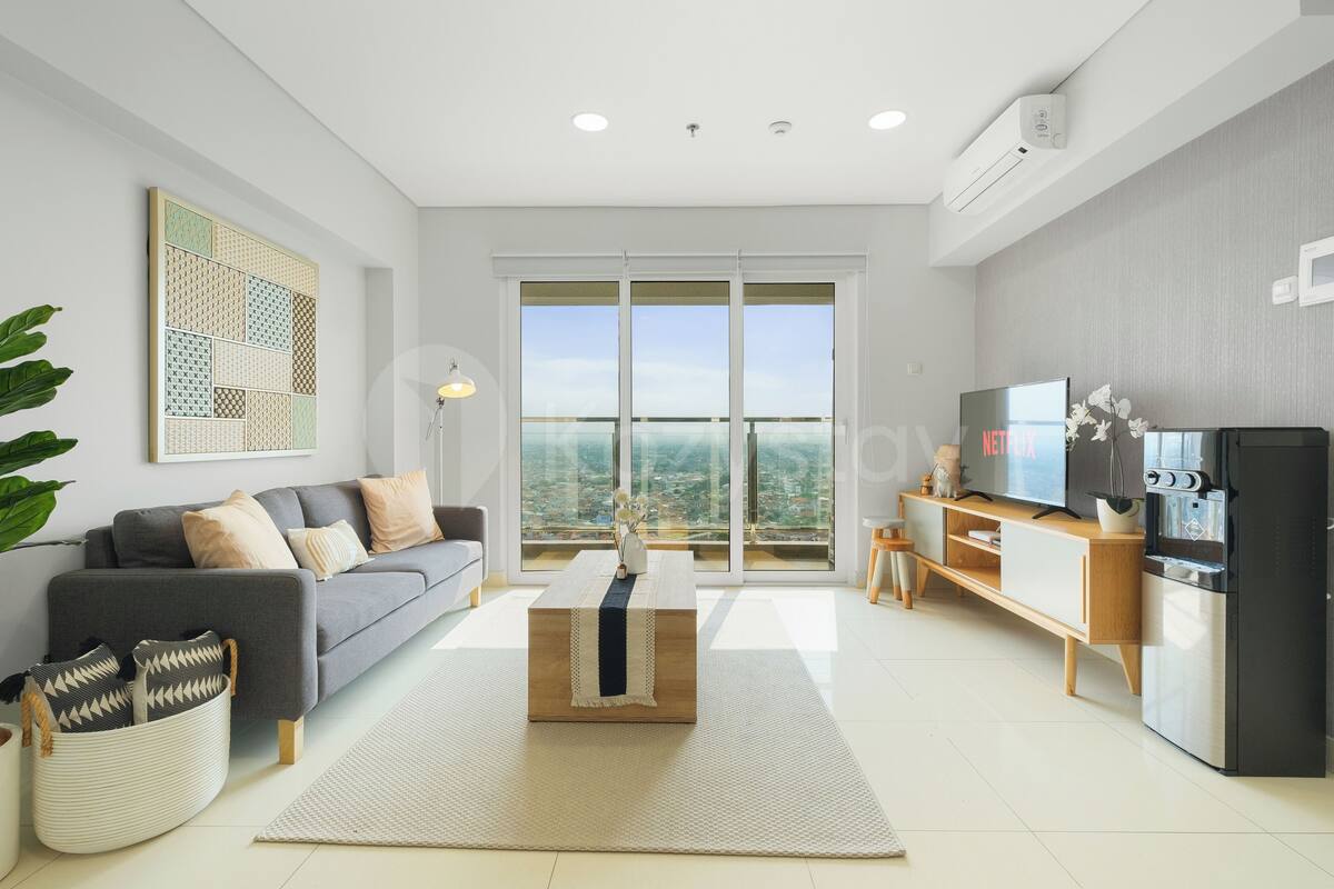 Una sala de estar moderna con un sofá gris, una mesa de centro, un televisor y una zona de cocina con refrigerador.