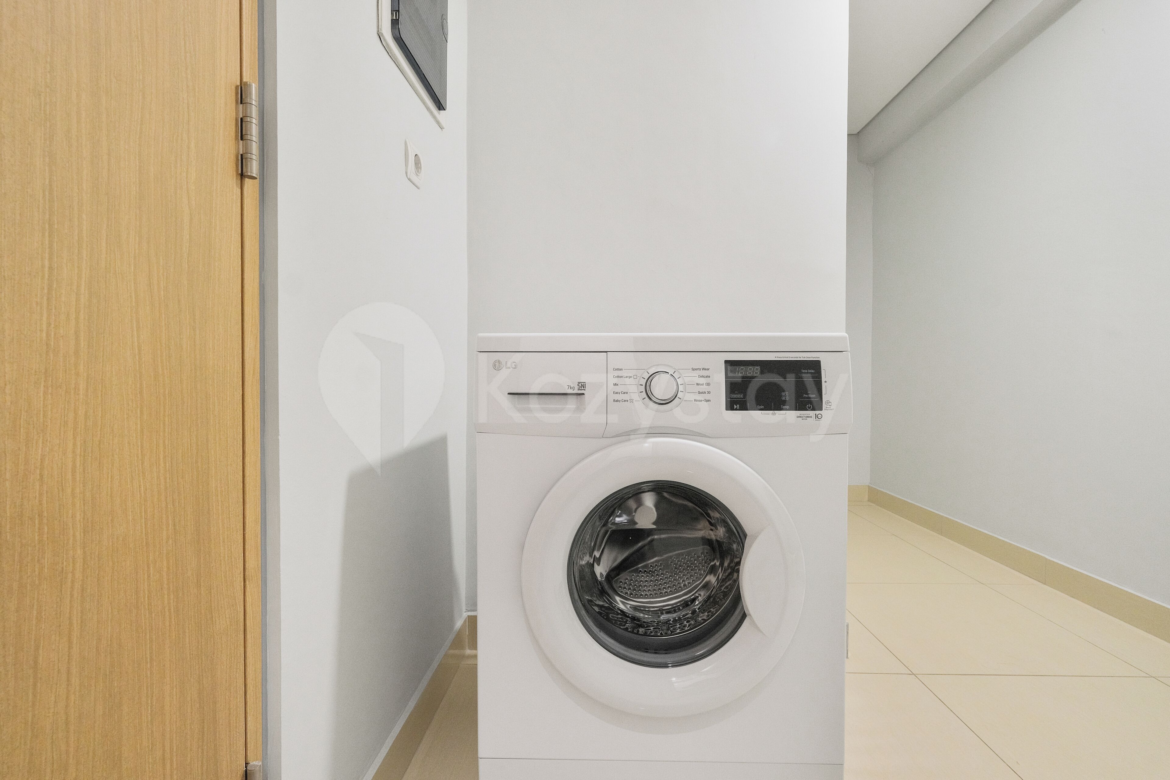 A white washing machine in a room with a wooden door and white walls.