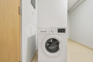 Una lavadora blanca en una habitación con una puerta de madera y paredes blancas.