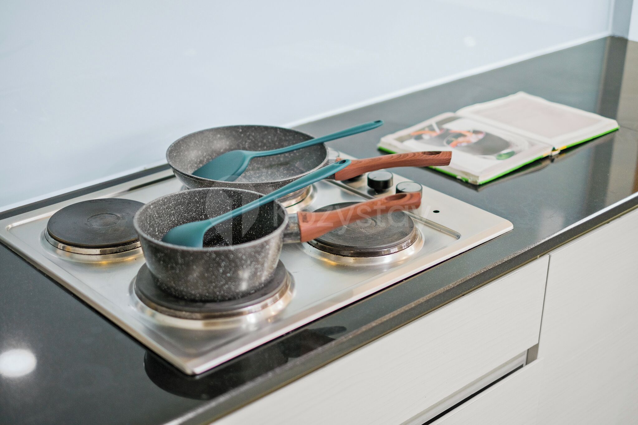 A kitchen with three pots on a stove, a cookbook, and a magazine on the counter.