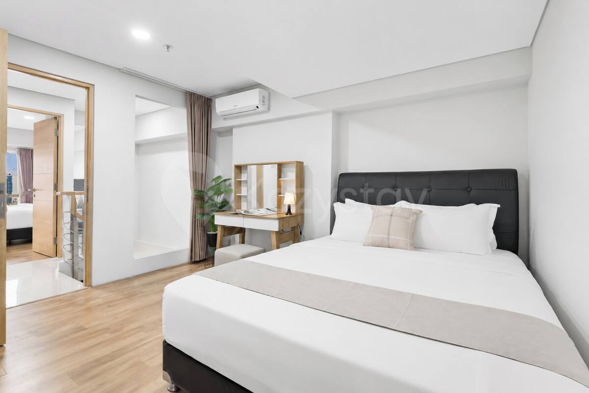 Una habitación de hotel moderna con una cama grande, un escritorio con silla, un espejo y un equipo de aire acondicionado.