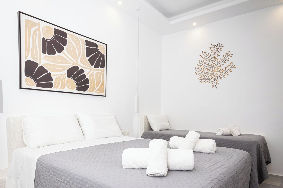 Quarto de hotel com uma cama grande, duas camas menores, uma obra de arte na parede e um detalhe decorativo na parede.