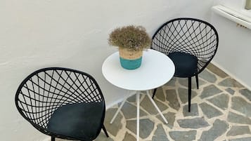 A small outdoor seating area with two black wireframe chairs and a white table, featuring a woven plant pot.