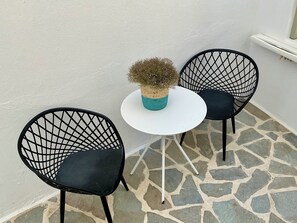 Un pequeño espacio al aire libre con dos sillas de estructura metálica negra y una mesa blanca, destacando una maceta tejida.