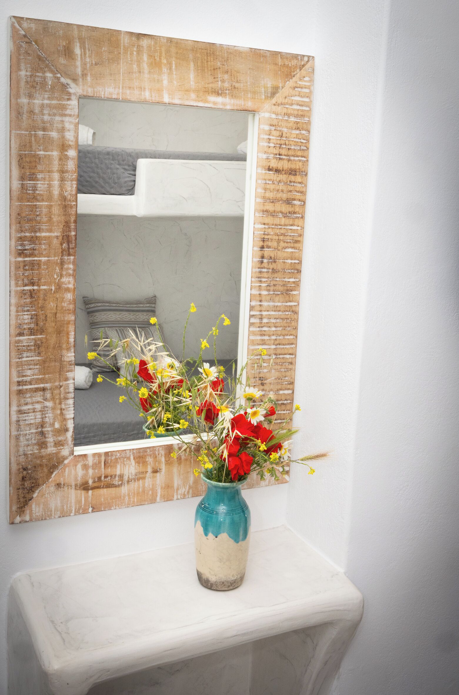 A bathroom with a white sink, a mirror with a distressed frame, and a vase with flowers on the sink.