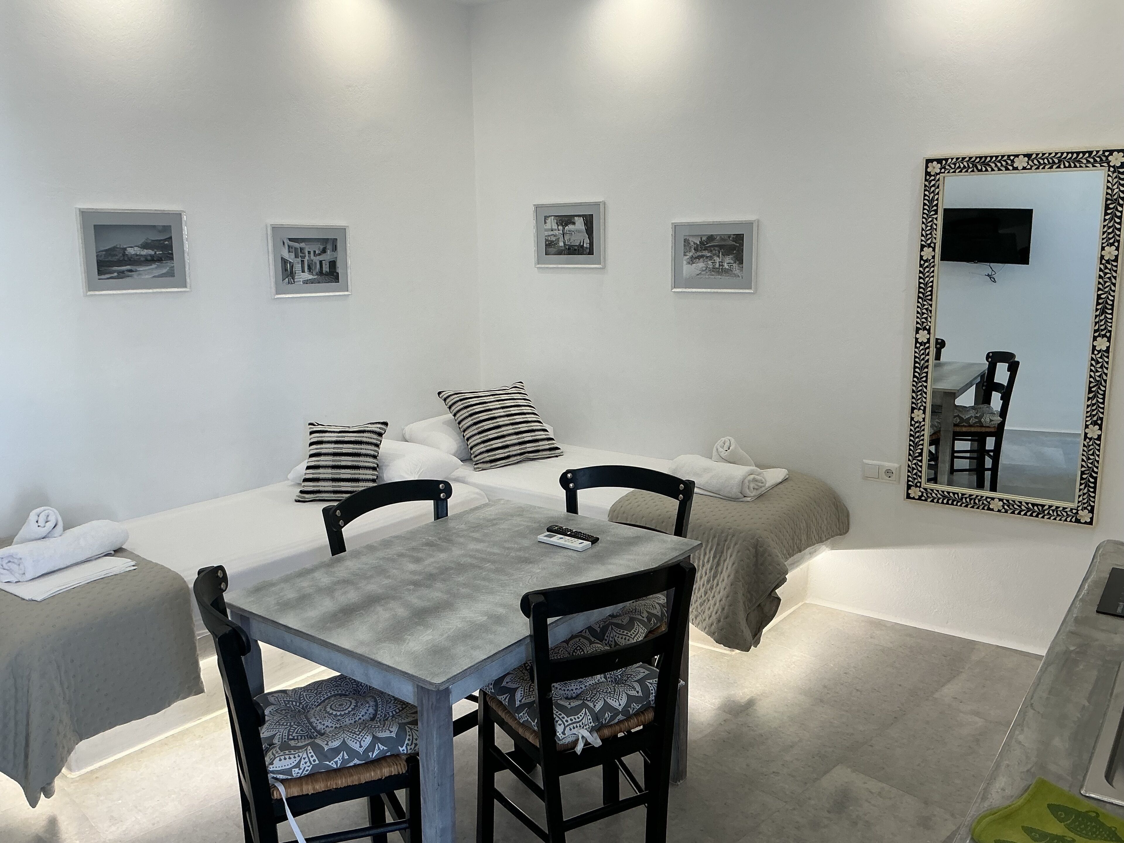A hotel room with a bed, two chairs, a table, a mirror, and four framed pictures on the wall.