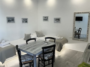 A hotel room with a bed, two chairs, a table, a mirror, and four framed pictures on the wall. - Ione Inn (Chora)