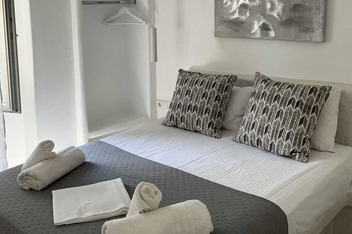Quarto de hotel com uma cama, duas almofadas estampadas, uma obra de arte na parede, um guarda-roupa e uma toalha sobre a cama.