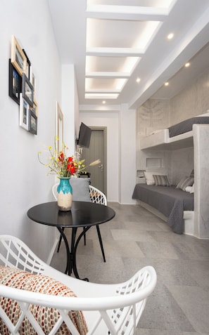 A compact room with a bunk bed, a round dining table with chairs, a vase with flowers, and a flat-screen TV mounted on the wall. - Ione Inn (Chora)