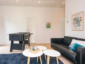 A living room with a foosball table, a black sofa, two white coffee tables, and a blue carpet. - 5 Star Holiday Home in Farvang (Farvang)