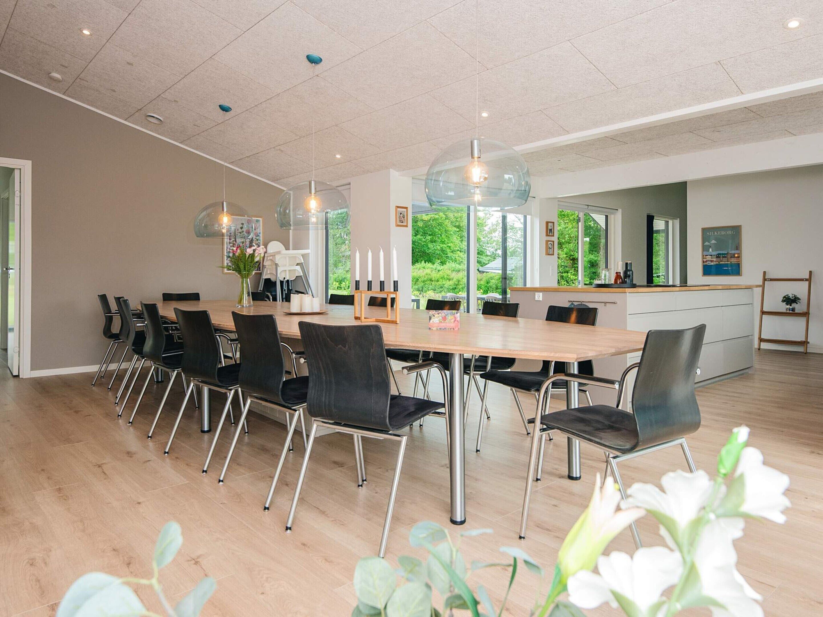Ein moderner Essbereich mit einem langen Tisch, schwarzen Stühlen und Pendelleuchten.