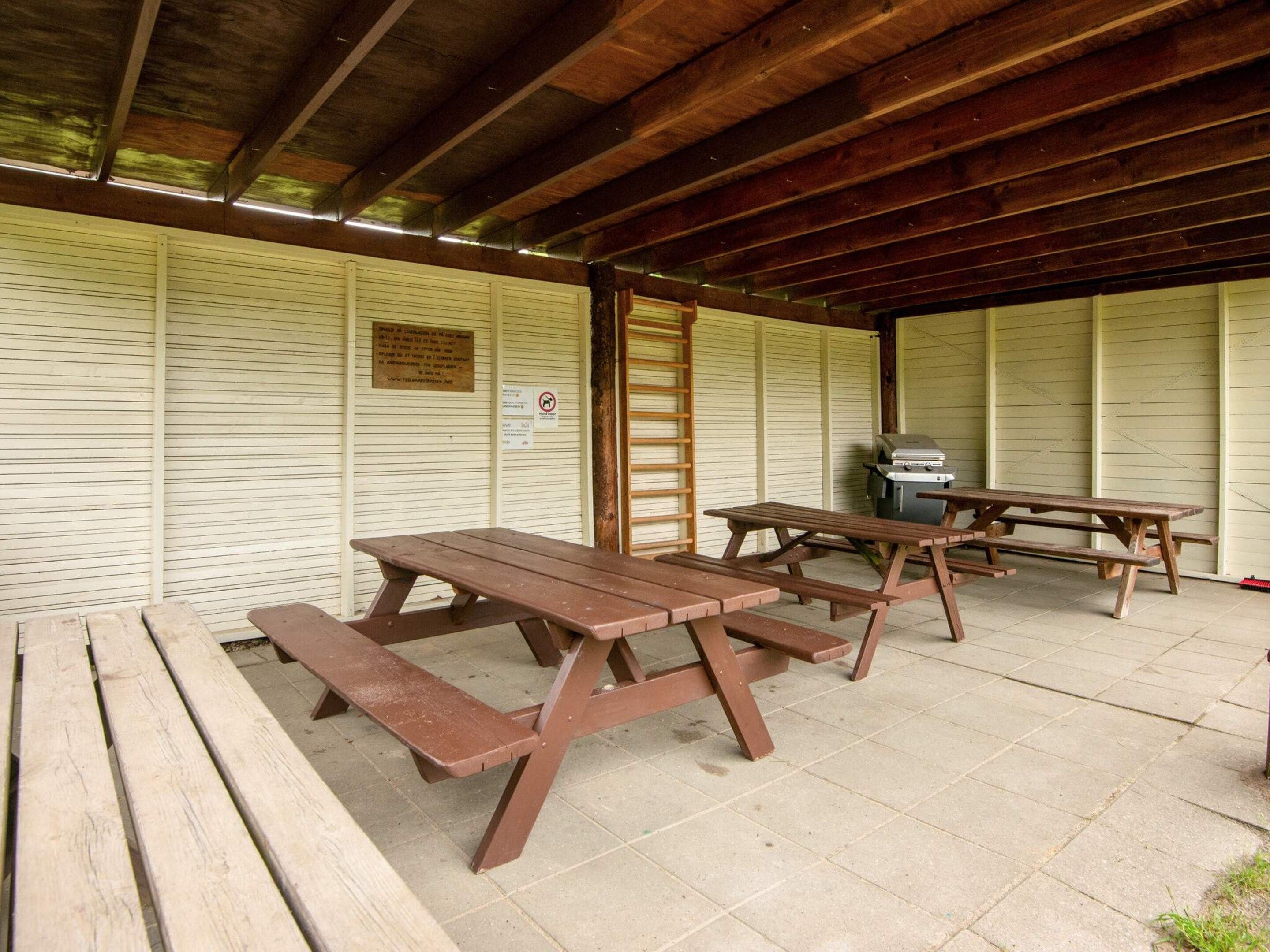Un espacio al aire libre techado con mesas de picnic y una parrilla.