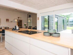 A modern kitchen with a central island, a dining area with chairs, and a view of a garden through large windows. - 5 Star Holiday Home in Farvang (Farvang)