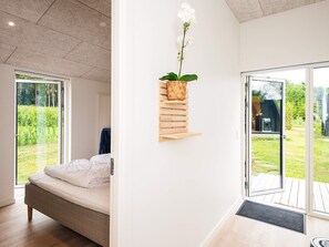 A bedroom with a bed, a wall-mounted shelf with a plant, and a sliding glass door leading to an outdoor area. - 5 Star Holiday Home in Farvang (Farvang)