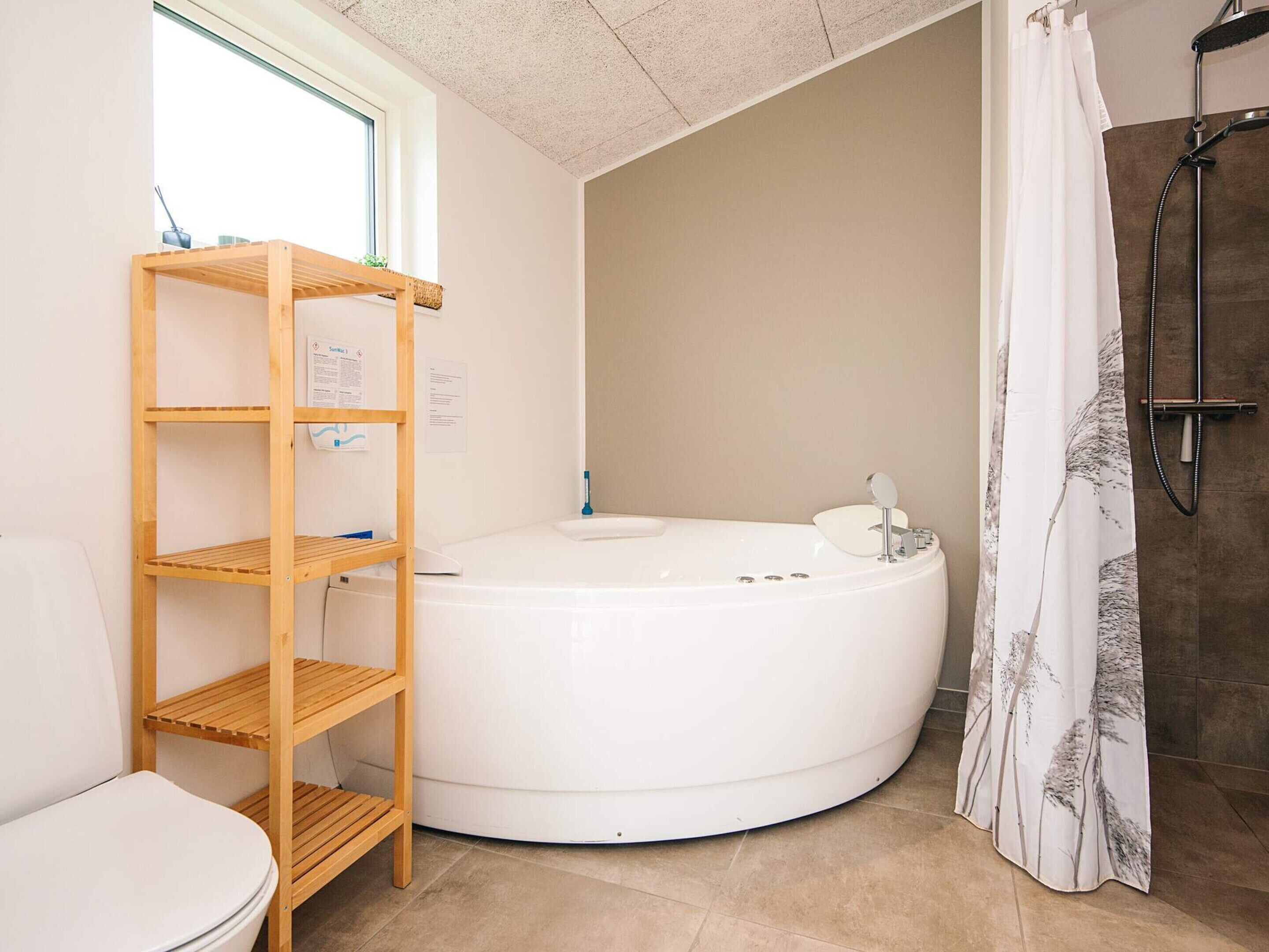 Un bagno con una vasca da bagno bianca, un mobiletto a mensole in legno, un water e una zona doccia con tenda.