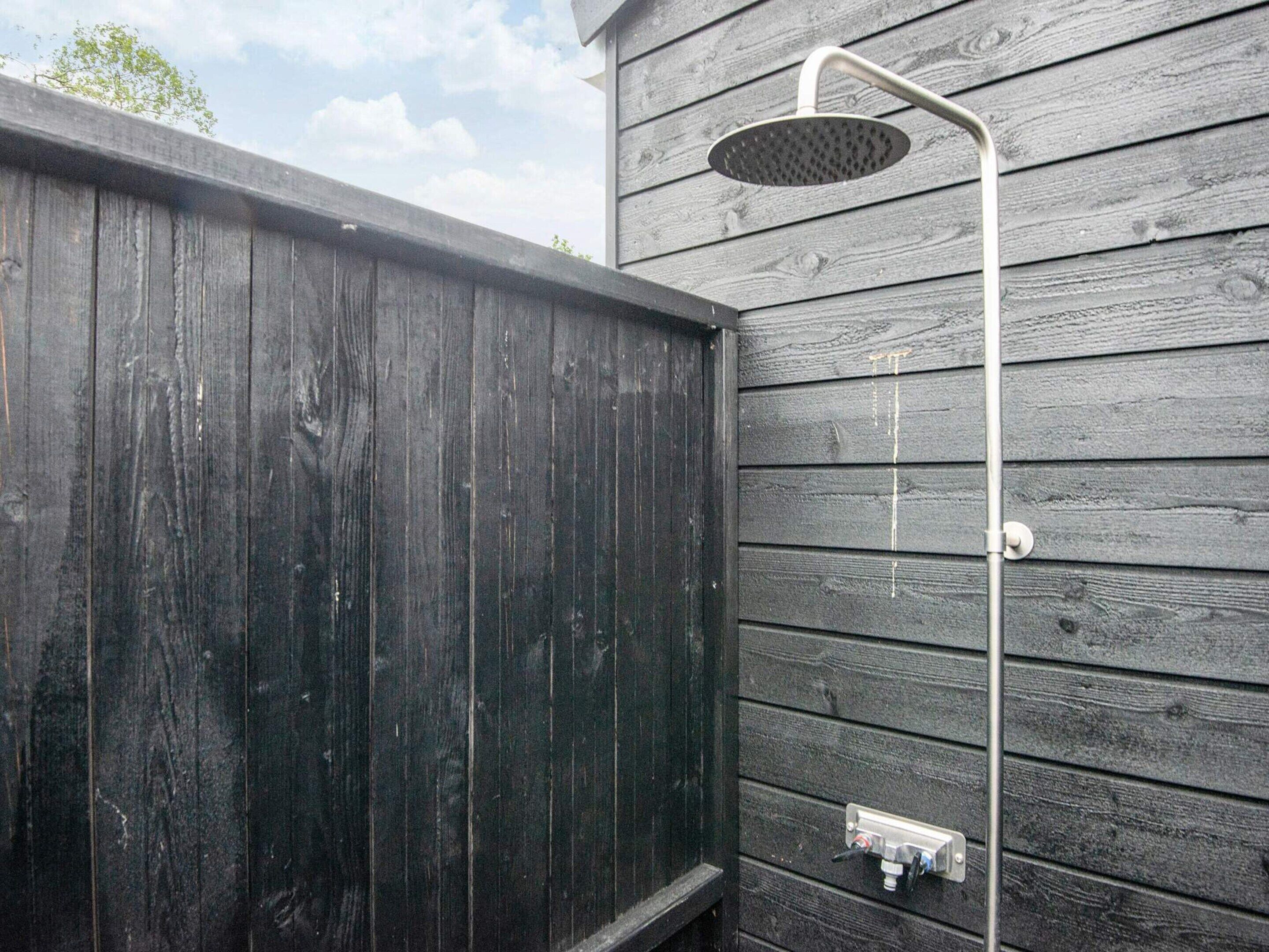 A wooden exterior wall with a metal showerhead attached to it.