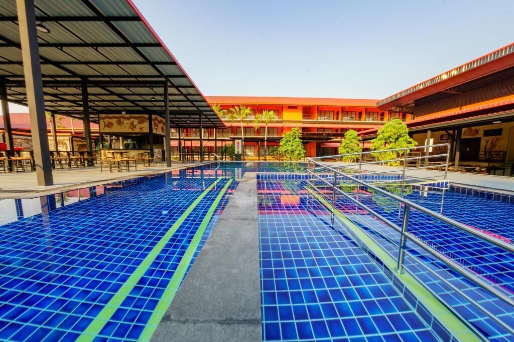 Una piscina con suelo de baldosas, rodeada por una zona cubierta con mesas y sillas.