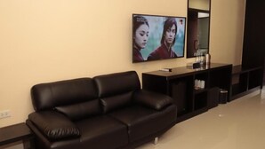 Una sala de estar moderna con un sofá de cuero negro, un televisor de pantalla plana montado en la pared, una pequeña consola y un espejo.