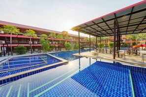 Ein Hotel mit mehreren Schwimmbecken, überdachten Sitzbereichen und einem Gebäude mit Balkonen.