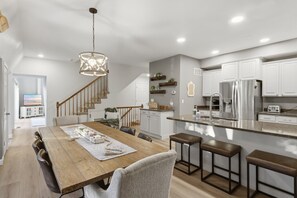 A modern kitchen with a wooden dining table, bar stools, a built-in island, and stainless steel appliances. - The Peak at Echo Valley - Hot Tub, 2 Slips, & Game Room! (Osage Beach)
