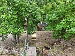 Eine steinerne Treppe führt zu einem Gebäude mit einer Holzterrasse, umgeben von üppigen, grünen Bäumen.