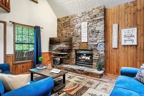 A cozy living room with a stone fireplace, blue sofas, and a television. - Beary Peaceful Smokies:Hot-Tub, Games & Pools (Pigeon Forge)