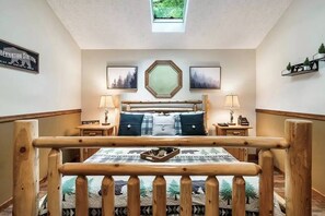 A bedroom with a wooden bed frame, a skylight, two bedside tables, and a wall-mounted mirror. - Beary Peaceful Smokies:Hot-Tub, Games & Pools (Pigeon Forge)