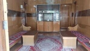 A room with wooden walls, a central cabinet with glass doors, two wooden benches, and patterned rugs. - Hotel Chubi Leh (Leh)