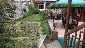 A garden area with a pathway, wooden benches, and a table with chairs. - Hotel Chubi Leh (Leh)