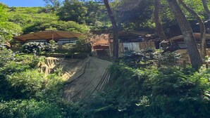 A rustic cabin surrounded by dense forest, with a covered outdoor seating area and a small structure nearby. - Cozzy Saprag Riverside Pangalengan (Pangalengan)
