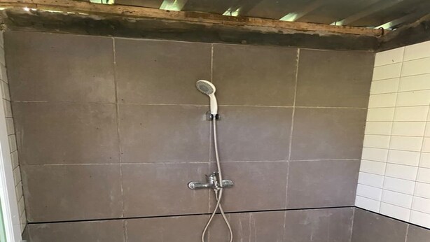 A small, enclosed shower area with a showerhead and hose, a white plastic basin, and tiled walls. - Cozzy Saprag Riverside Pangalengan (Pangalengan)