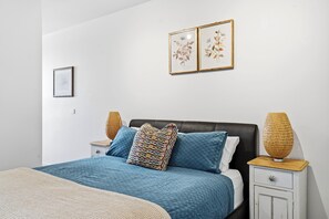 Ein Schlafzimmer mit einem Bett, zwei Nachttischen, einer Kommode, einer Wandlampe und zwei gerahmten Bildern.