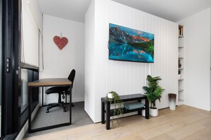 Ein modernes Zimmer mit Schreibtisch, Stuhl, Fernseher, herzförmiger Dekoration und Topfpflanzen.