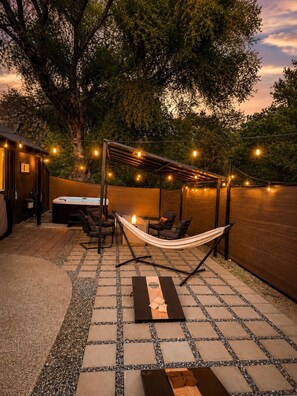 Een terras met een hangmat, zitplaatsen en een barbecueplaats, omgeven door een houten omheining en bomen.